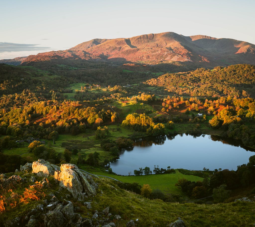 A panoramic view of a serene lake surrounded by lush hills during a vibrant sunset.