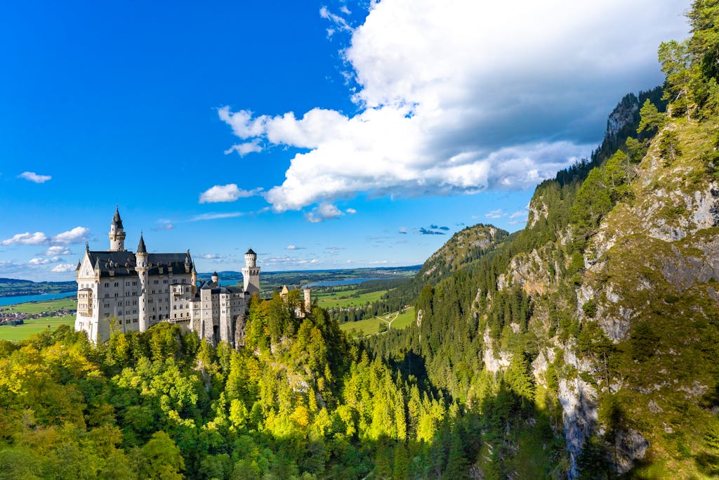 Aerial view of Neuschwanstein Castle in Bavaria, Germany, surrounded by lush forests and mountains under a blue sky.