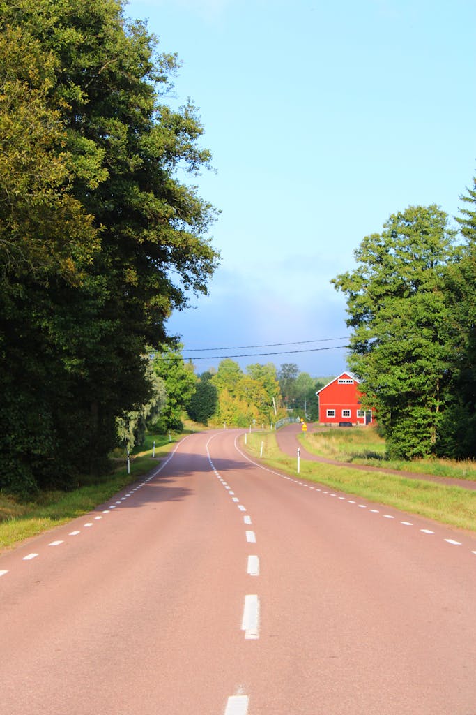 Charming countryside road in Åland, leading past a vibrant red house surrounded by lush greenery.