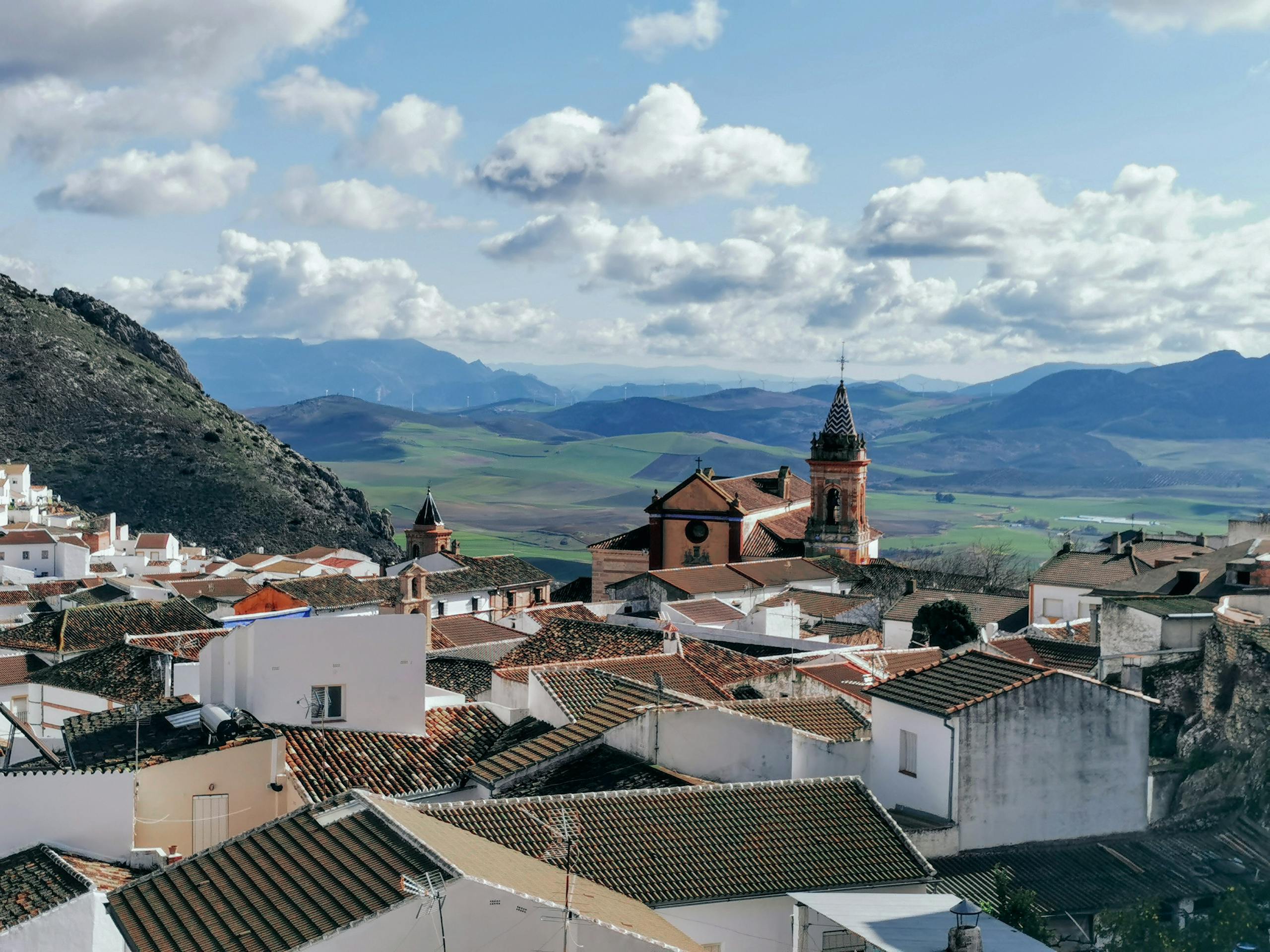 Discover the charming rooftops and majestic church in Cañete la Real, Spain, against a mountainous backdrop.