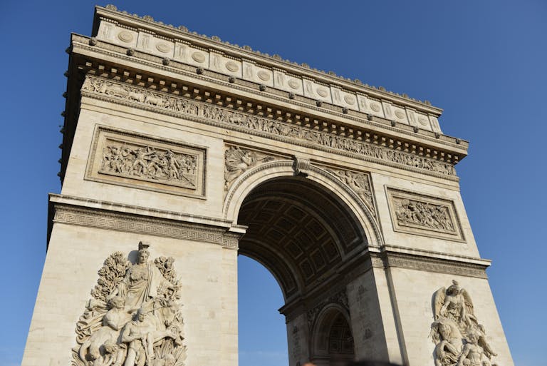 Low angle shot of the iconic Arc de Triomphe in Paris set against a clear blue sky.