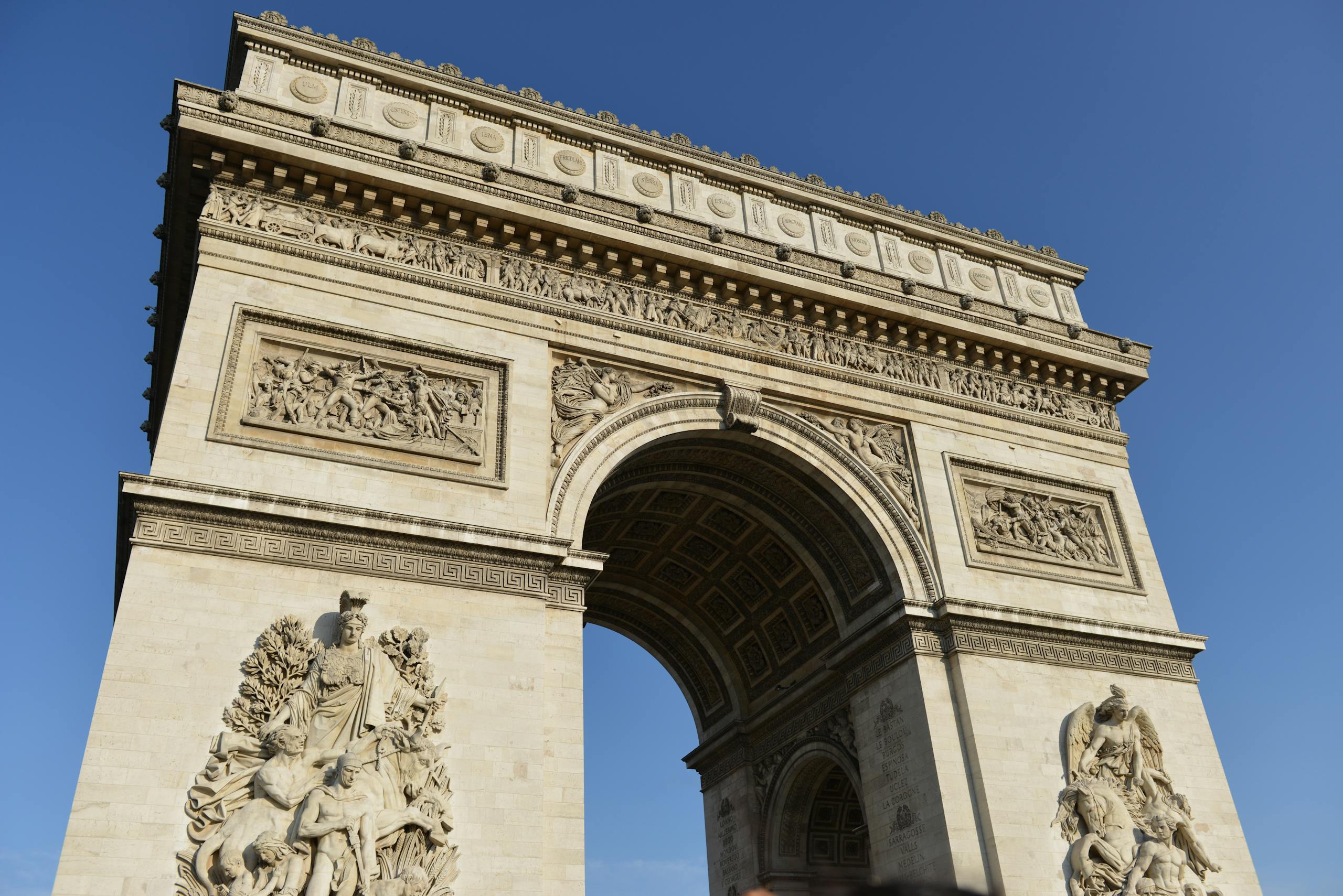 Low angle shot of the iconic Arc de Triomphe in Paris set against a clear blue sky.
